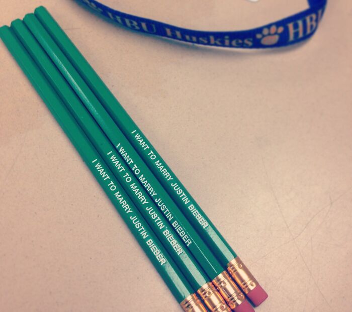 Green pencils with pink erasers lying on a desk, each engraved with a funny teacher phrase about Justin Bieber.