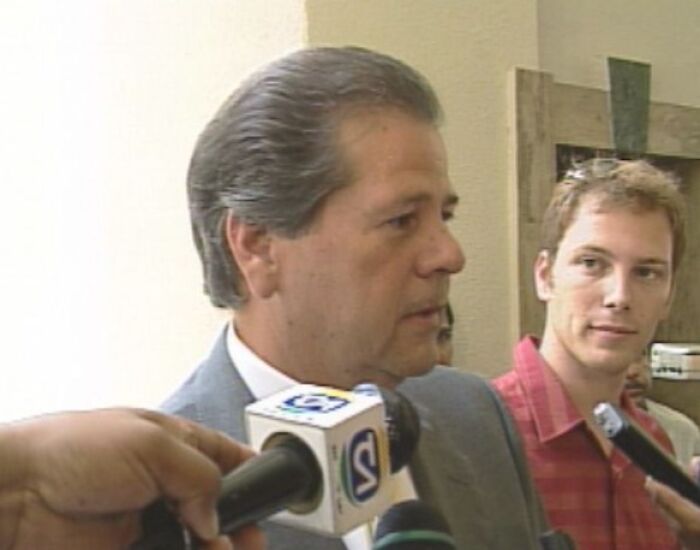 Man in a suit speaking to reporters with microphones during an interview about famous fraud cases.