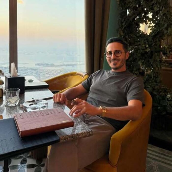 Man with glasses and watch sitting at a table in a restaurant, representing famous fraud cases and luxury lifestyle.