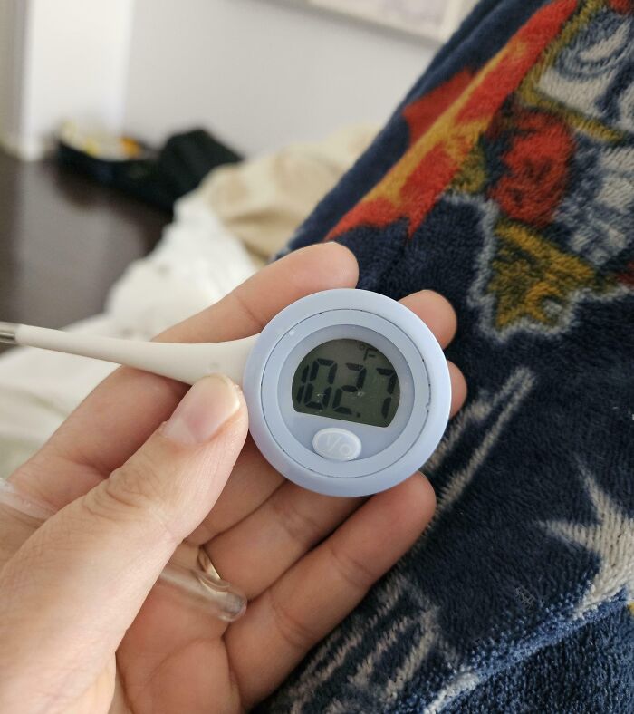Hand holding a digital thermometer showing a fever while resting on a colorful blanket, illustrating bad vacation luck.
