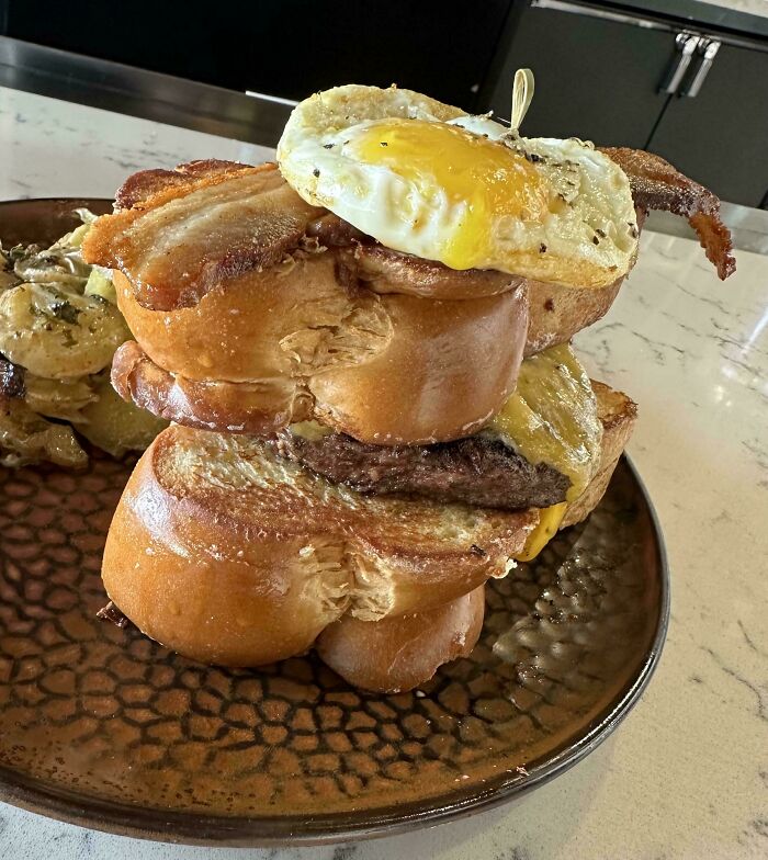Stacked burger with fried egg, bacon, and thick bread slices served on a plate among dishes from stupid dishes collection