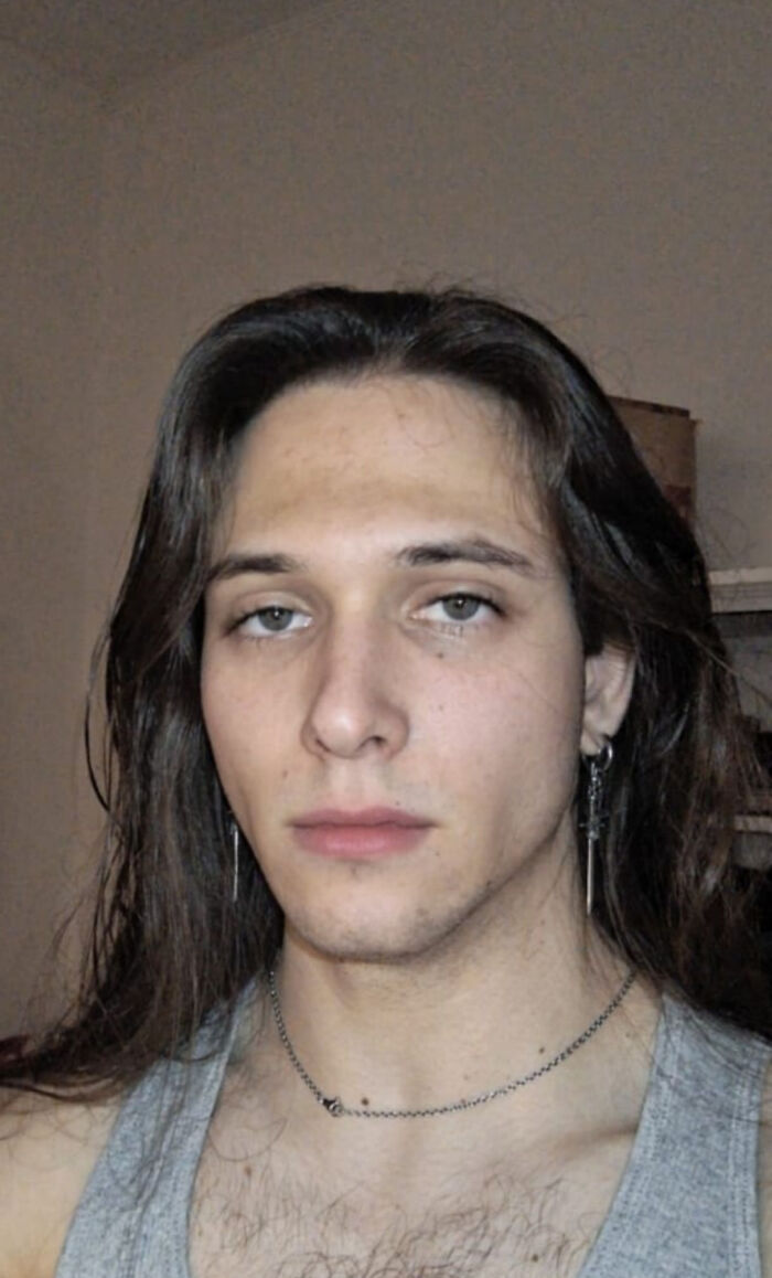 Young man with fierceflow hairstyle and long beautiful hair wearing earrings and a gray tank top in a casual indoor setting