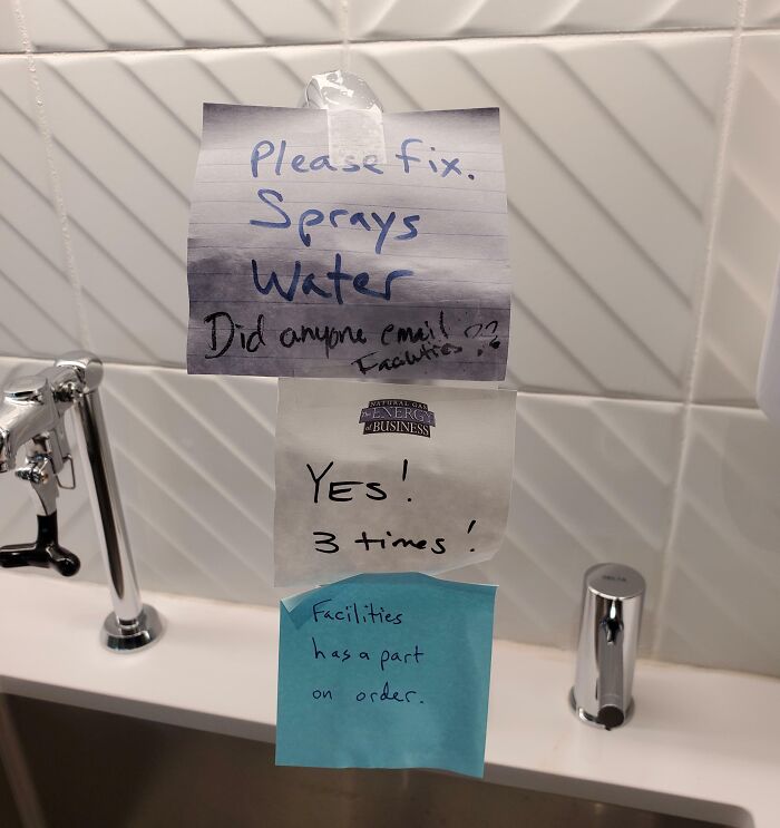 Passive-aggressive notes from coworkers about a broken spray water fixture with multiple responses stuck above a sink.