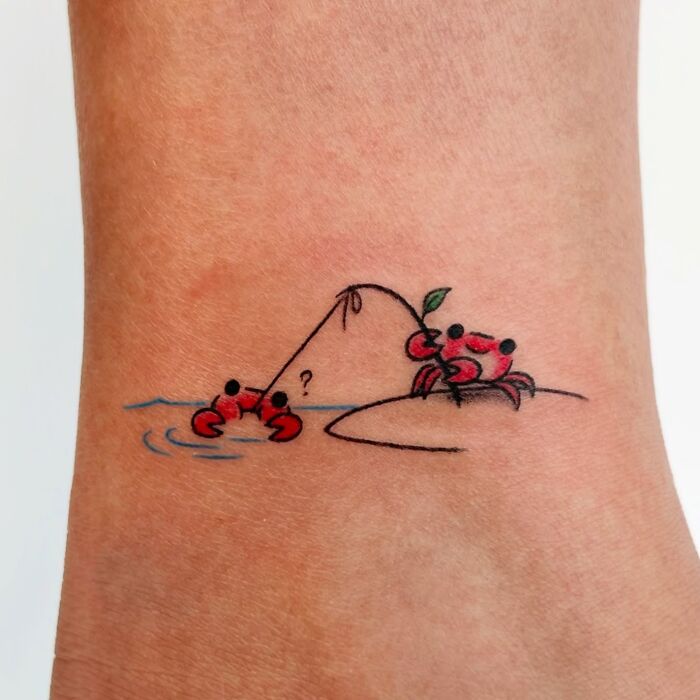 Minimalist crab tattoo on wrist showing one crab fishing with a leaf, part of adorable animal tattoos by Korean artist Buoy.
