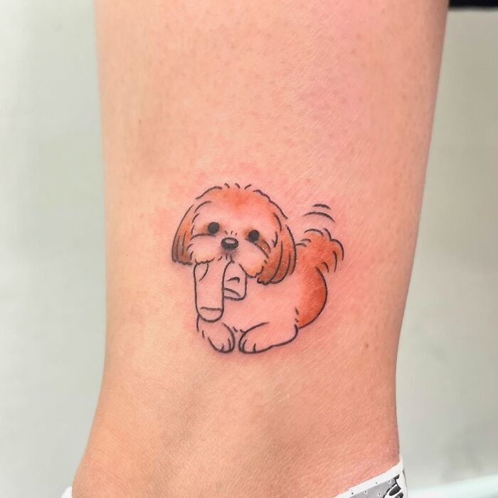 Small adorable animal tattoo of a playful dog holding a sock, featuring delicate lines and soft shading by Korean artist Buoy.