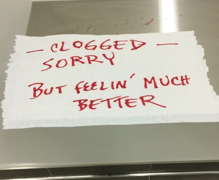 Passive-aggressive note on torn paper in red ink about a clogged item, showing coworker frustration.