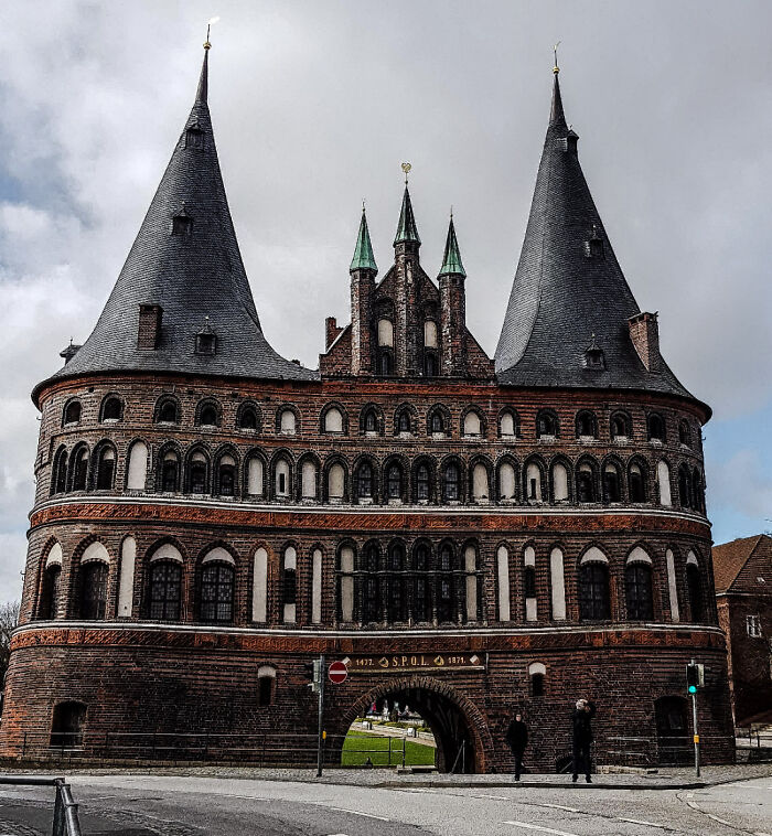 The Holstentor, a beautiful brick architecture gate with two towering spires, stands majestically under a cloudy sky.