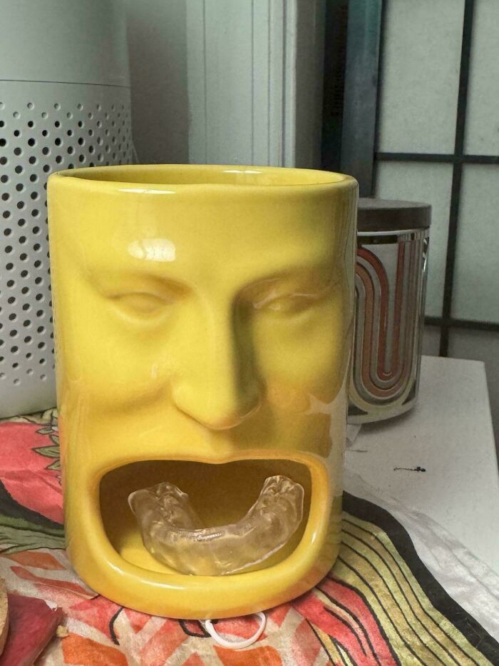 Yellow ceramic face-shaped holder with a clear dental retainer displayed as a unique thrift store find.