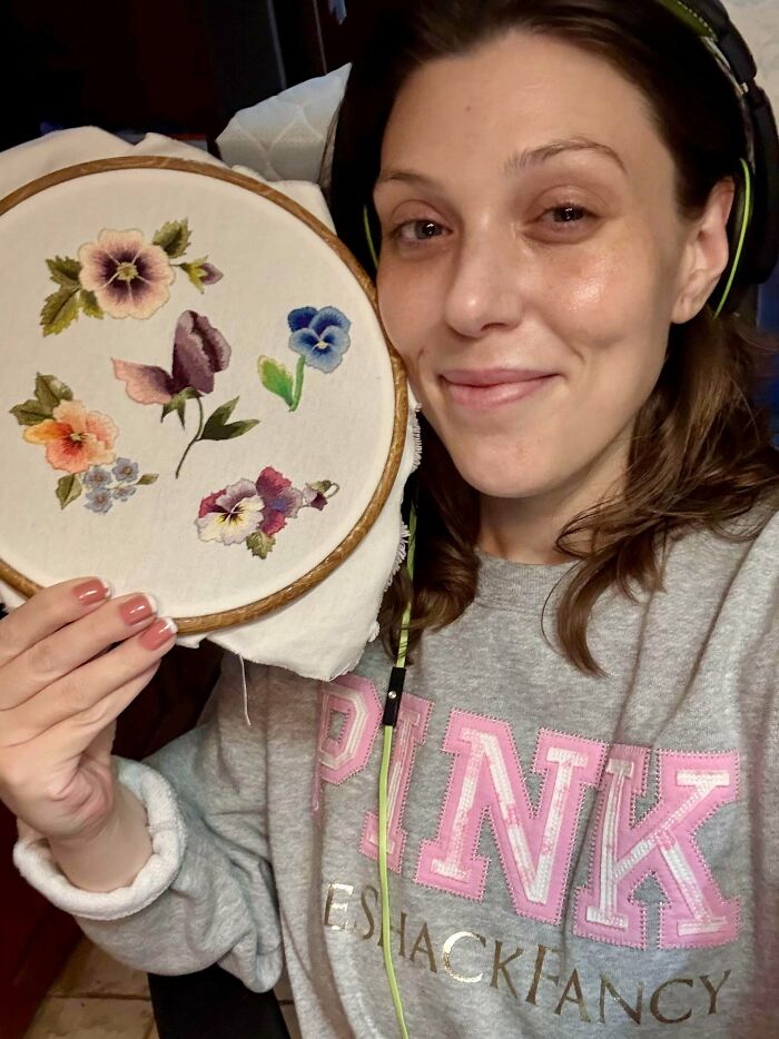 A woman smiling and holding a stunning embroidery creation of colorful flowers in a hoop, inspiring embroidery creations.