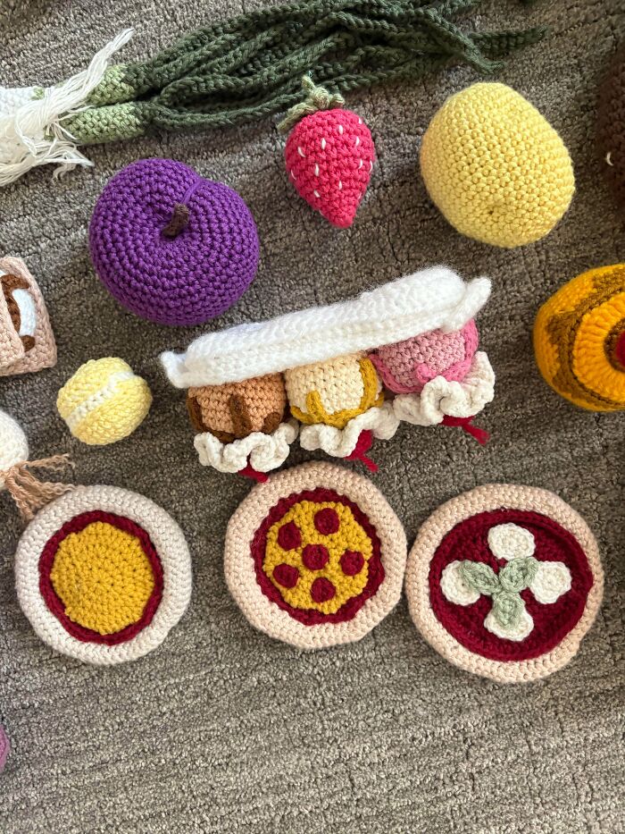 Crocheted fruits and mini pizzas arranged on a carpet showcasing creative crocheting projects by skilled crafters.