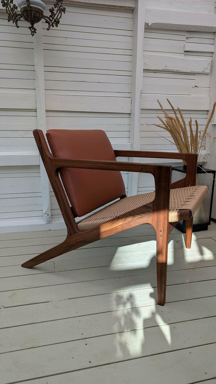 Mid-century modern woodworking chair with leather backrest and woven seat on a white wooden floor.
