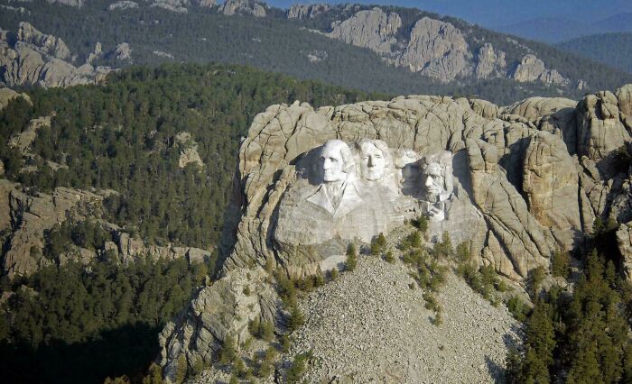 Mount Rushmore National Memorial carved into granite with surrounding pine forest and distant mountain backdrop.