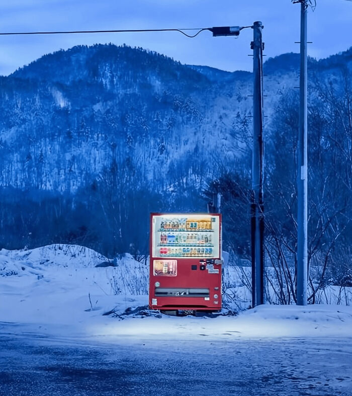 Red vending machine glowing in snowy landscape at dawn with mountains and early Devil Sunrise light in background.