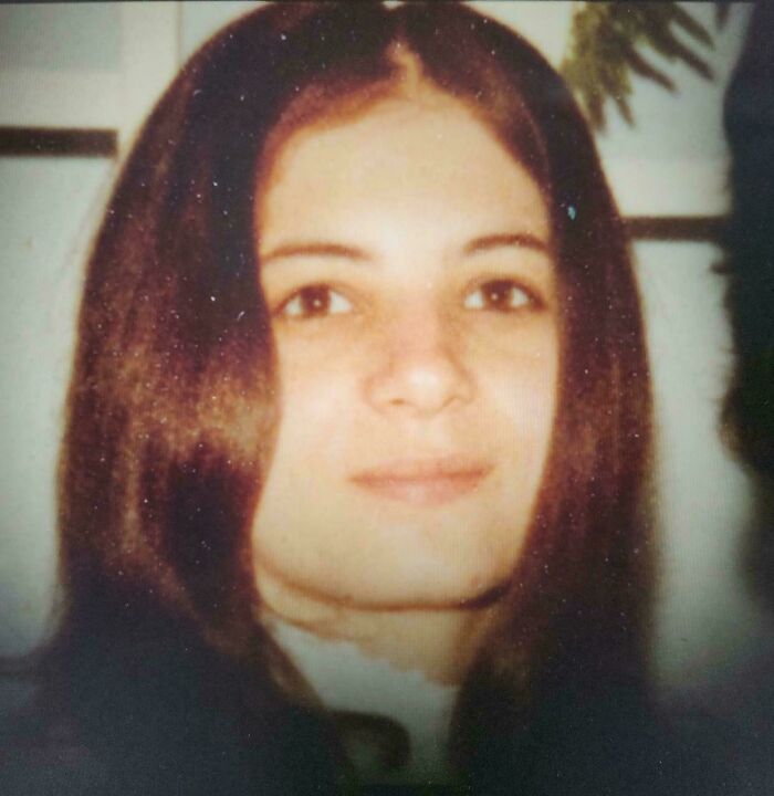Young woman with long brown hair, softly smiling in a vintage-style photo, still remains undiscovered to this day.