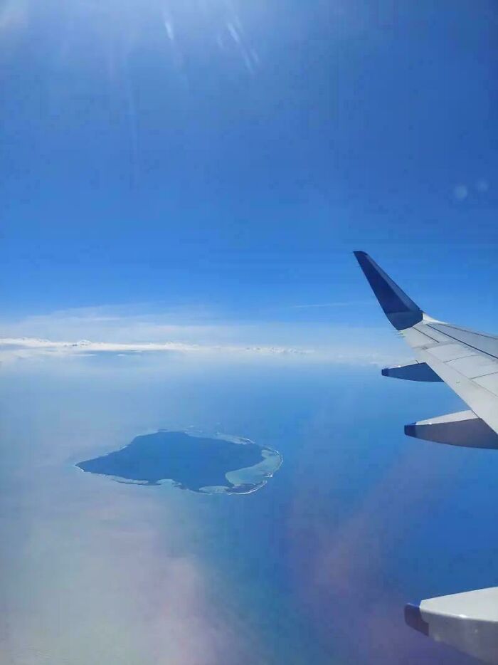 View of a remote island still remains undiscovered to this day captured from an airplane window under clear blue skies.
