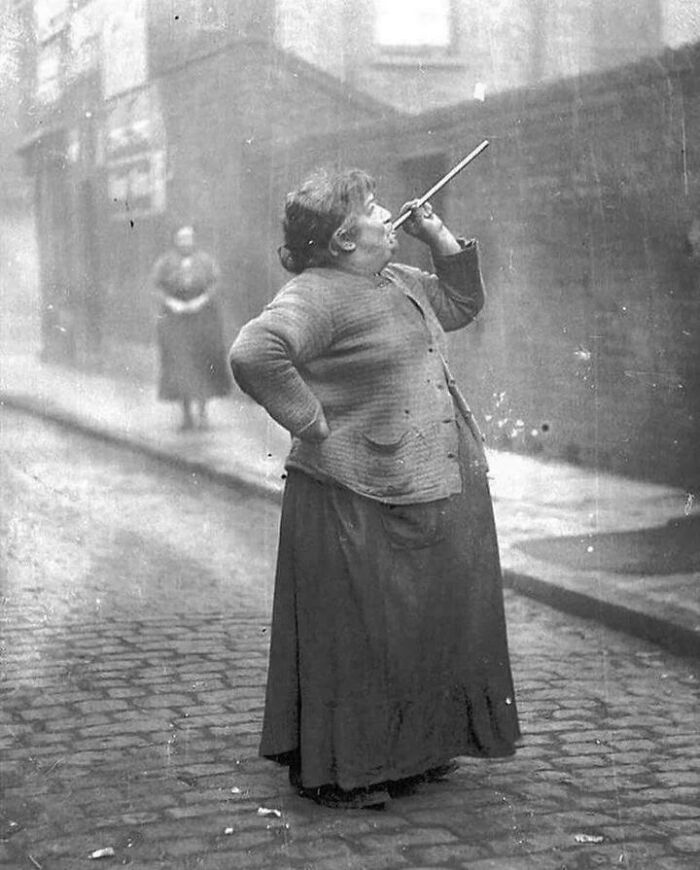 Vintage black and white photo of a woman smoking a pipe on a cobblestone street, still remains undiscovered to this day.