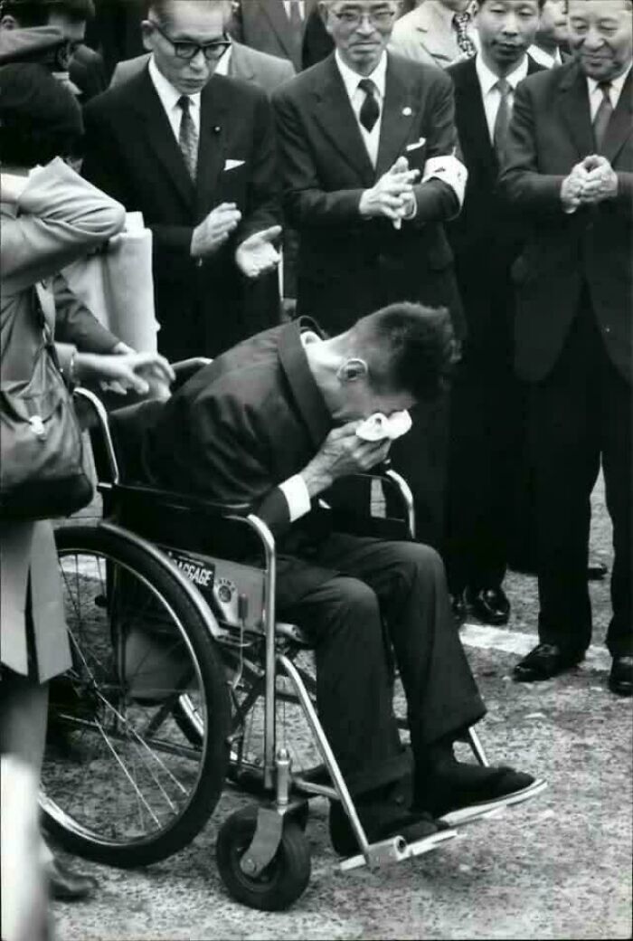 Black and white photo of a man in a wheelchair surrounded by people, capturing a still remains undiscovered moment.