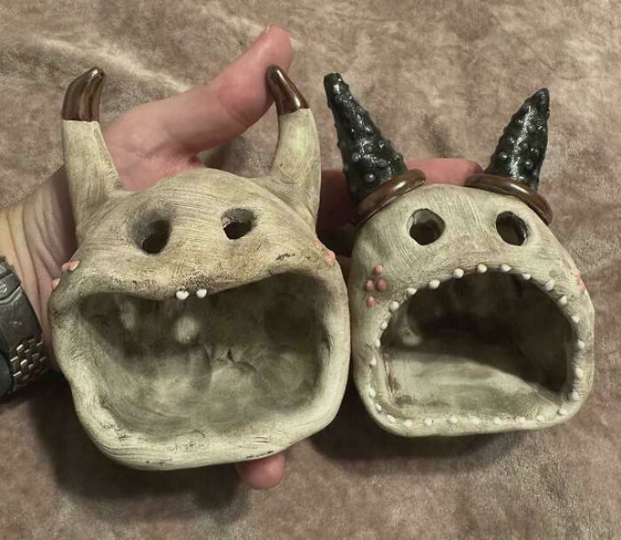 Hand holding two unique handcrafted ceramic thrift store finds shaped like whimsical creatures with open mouths and horns.