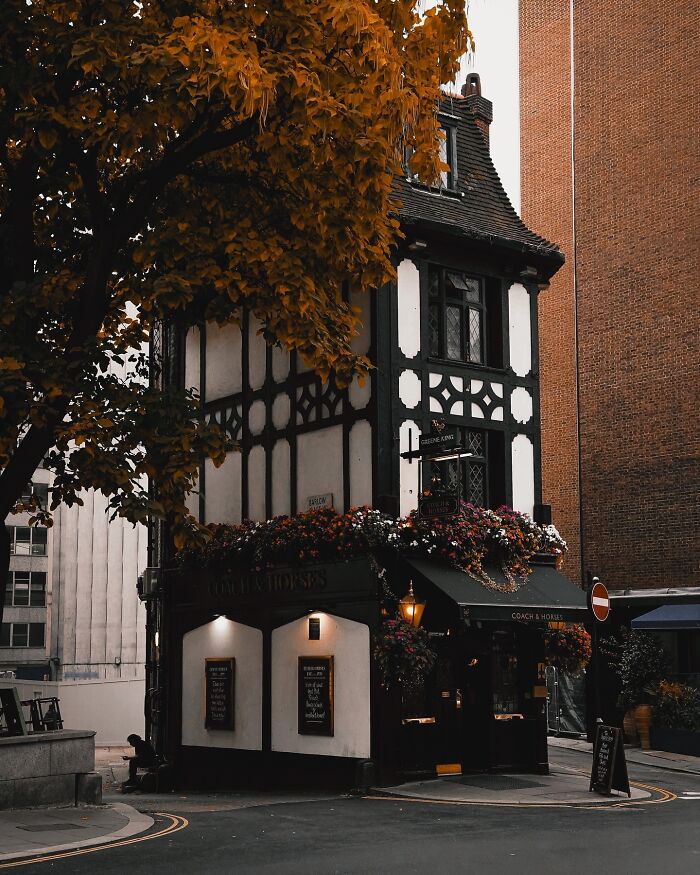 A charming old pub with beautiful architecture, black-and-white timber framing, and colorful flowers under an autumn tree.