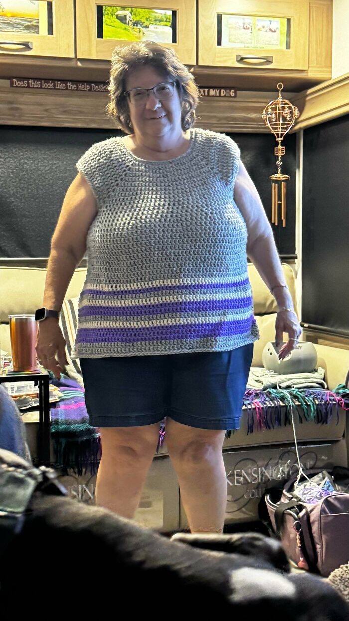 Woman wearing a handmade crochet top with purple stripes, showcasing a creative crocheting project inside a cozy room.