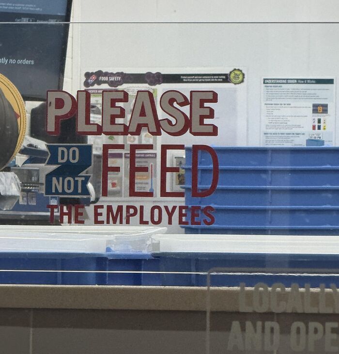 Sign reading please do not feed the employees in a restaurant window, reflecting a dystopian US real-life scene.