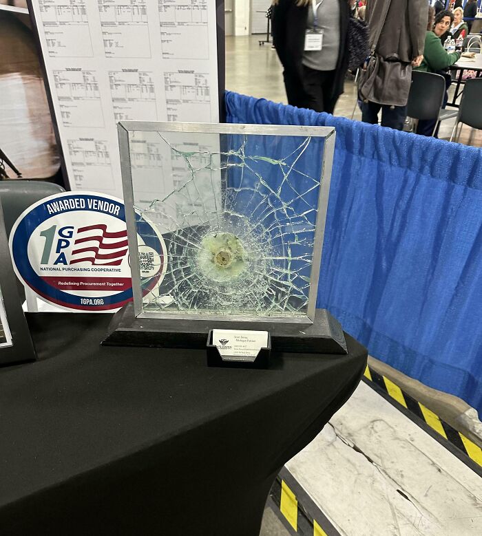 Shattered bulletproof glass panel on display at an event, illustrating real-life dystopian security concerns in the US.