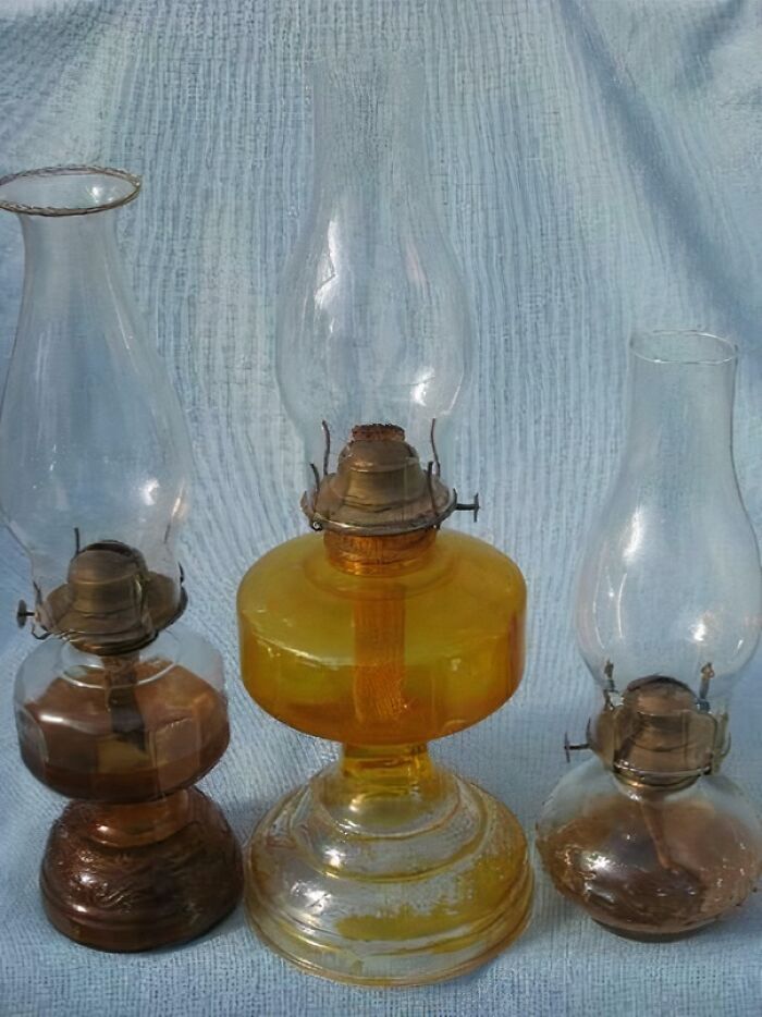 Three vintage oil lamps with glass chimneys displayed on a fabric background, evoking nostalgia and old age memories.
