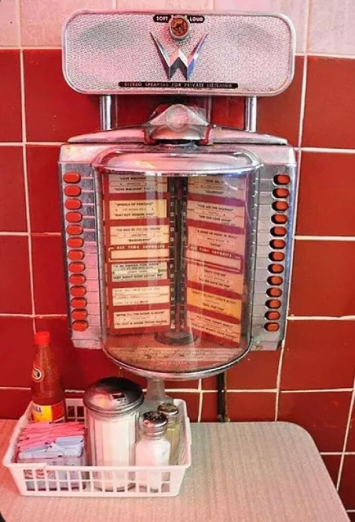 Vintage jukebox menu selector with nostalgic red tiles and classic diner condiments on a table, evoking old age memories.