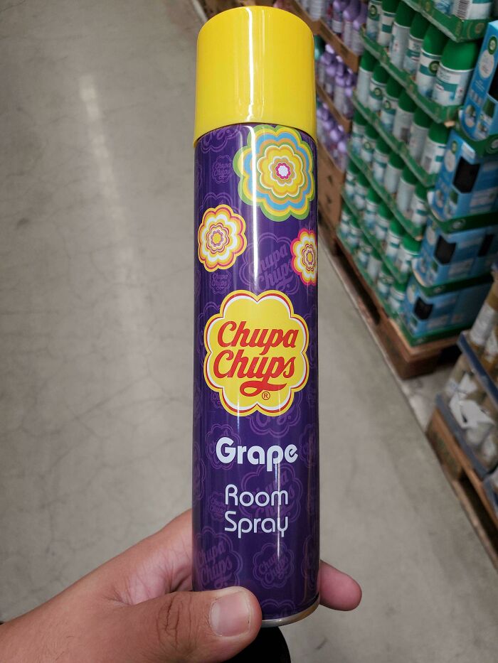 Hand holding a Chupa Chups grape room spray can in a store aisle filled with various products, nonsensical things that exist.