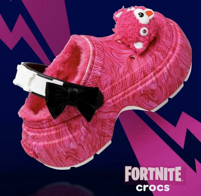 Pink nonsensical Crocs shoe with a furry interior, cartoon character, and black bow, showcasing quirky fashion trends.