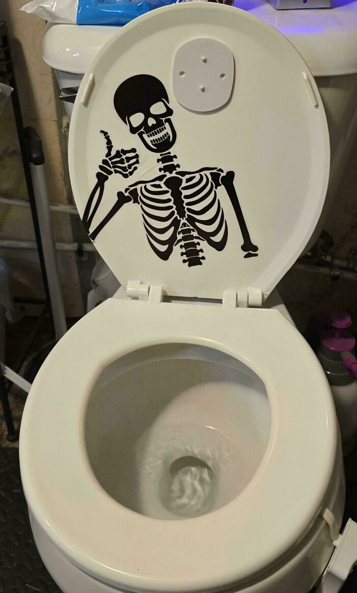 Toilet seat with a skeleton decal giving a thumbs up, showcasing one of the most nonsensical things that actually exist.
