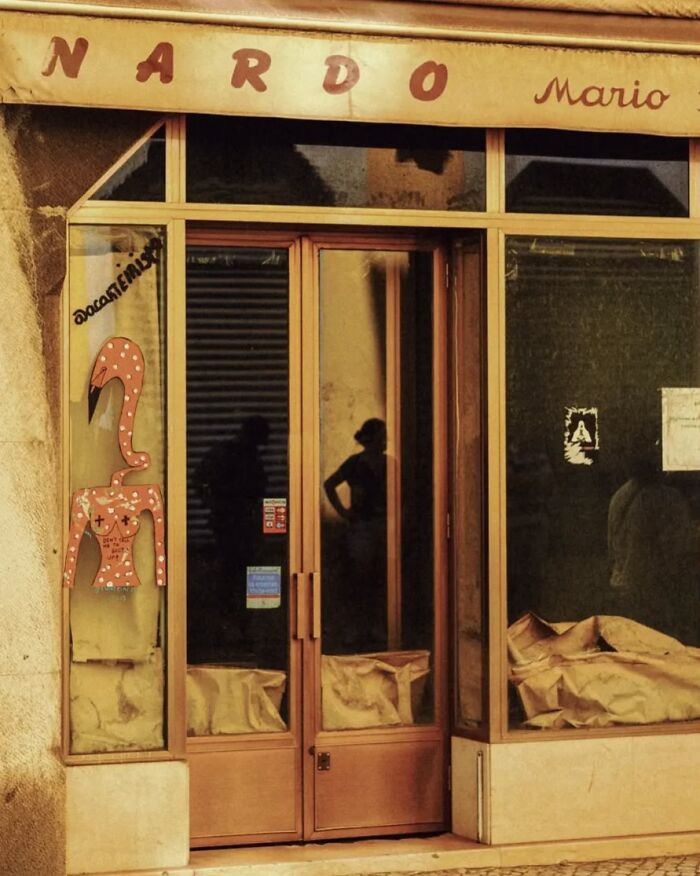 Street photo capturing a rustic storefront with reflections and shadow figures by Greek photographer Marina Nota.