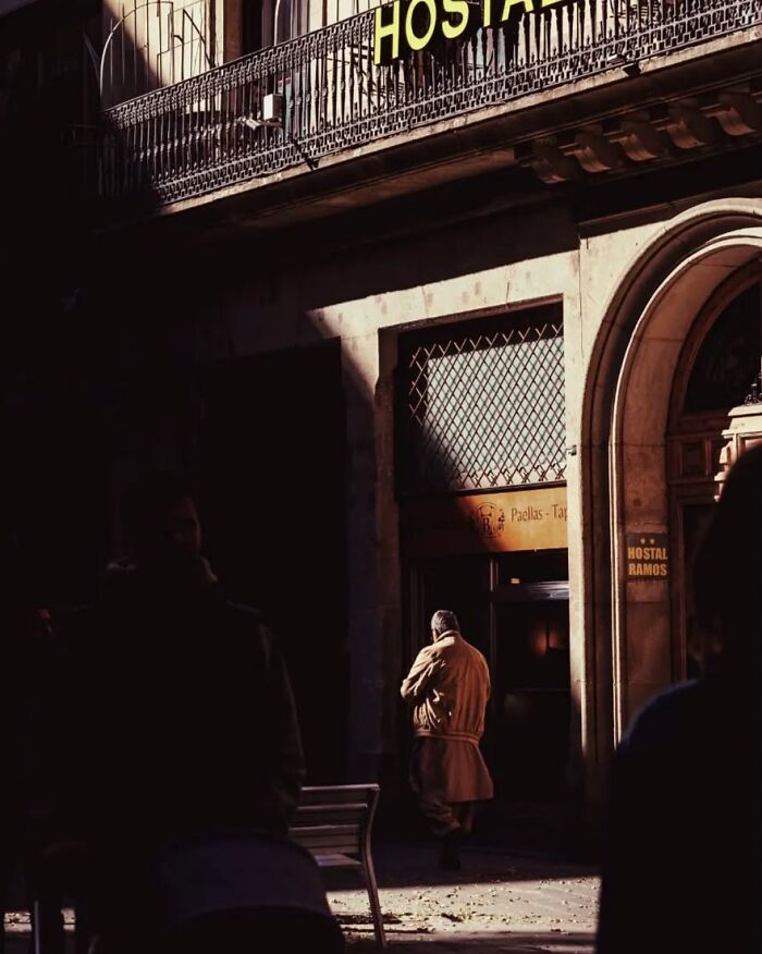 Street photo by Greek photographer Marina Nota showing a person walking near a sunlit building entrance.