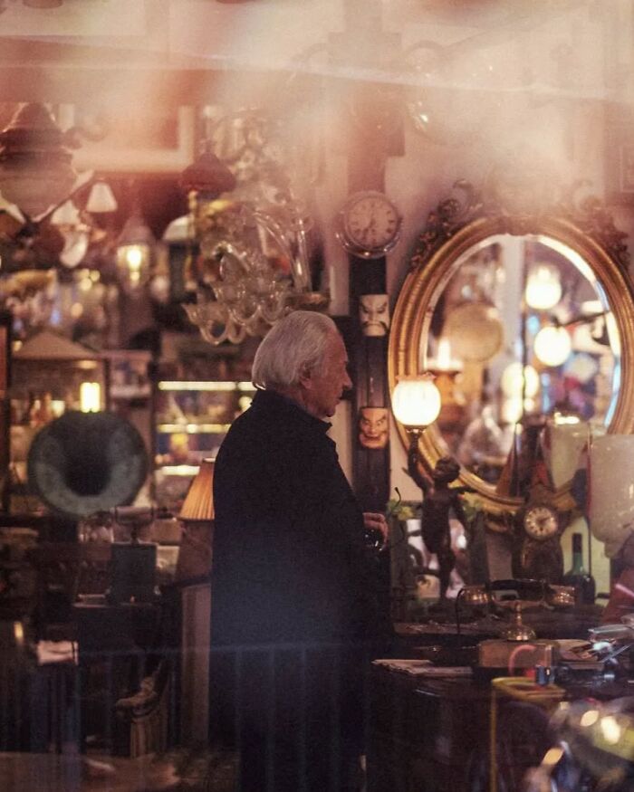 Elderly man in a vintage shop surrounded by antique items in a stunning street photo by Greek photographer Marina Nota.