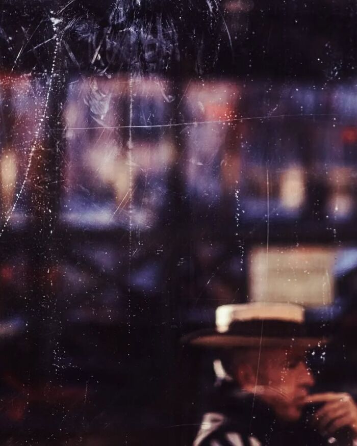 Blurred street photo featuring a person in a hat seen through a scratched glass window, showcasing stunning street photography.