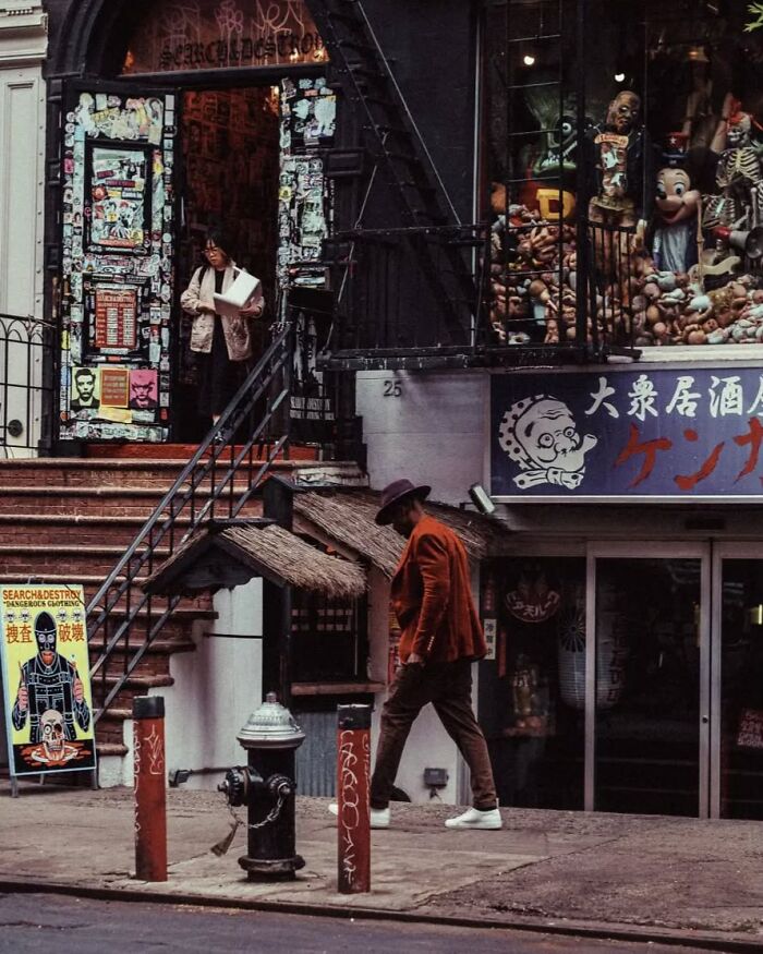 Man in brown jacket and hat walking past a quirky urban storefront in a stunning street photo by Greek photographer Marina Nota.