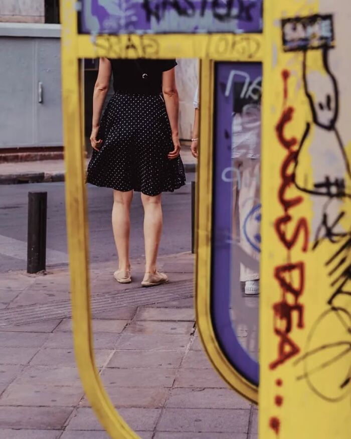 Woman wearing black polka dot skirt walking on urban sidewalk captured in striking street photo by Greek photographer Marina Nota.