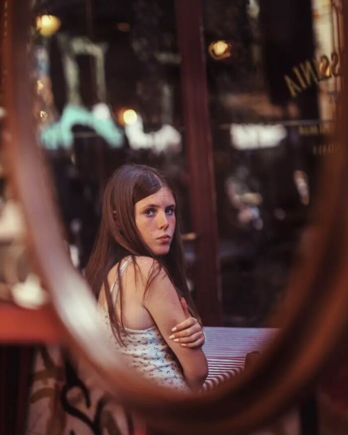Young woman with long hair captured in a street photo by Greek photographer Marina Nota, reflected in a round mirror.