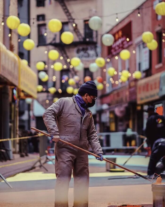 Street photo of a masked worker painting a city street, captured by Greek photographer Marina Nota.