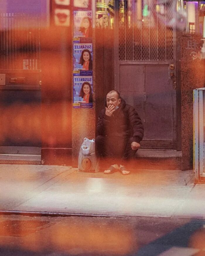 Man sitting on street step smoking a cigarette with shopping bag nearby in a stunning street photo by Greek photographer.