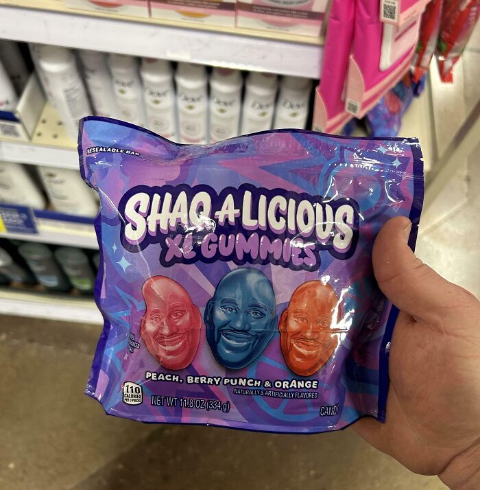 Hand holding a bag of Shaq A Licious XL Gummies with peach, berry punch, and orange flavors in a store aisle.
