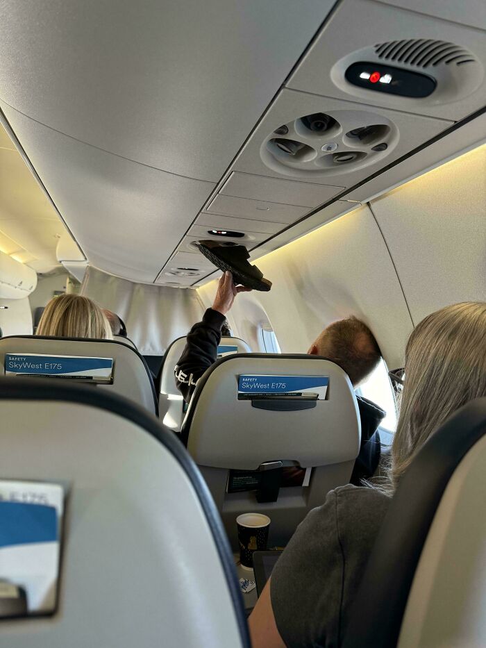 Passenger on a plane holding a shoe to the air vent, showing people allergic to acting like sensible adults in public.