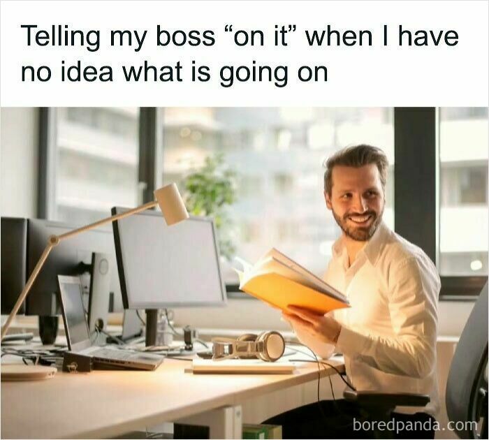 Man smiling at his desk holding a book, illustrating a painful and spot-on work meme about confusion in the office.