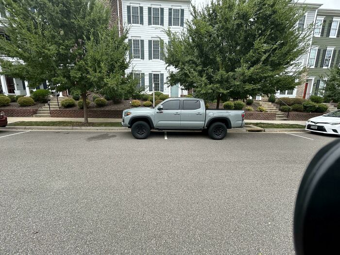 Silver pickup truck parked across two spaces in a residential area, illustrating people allergic to acting like sensible adults.