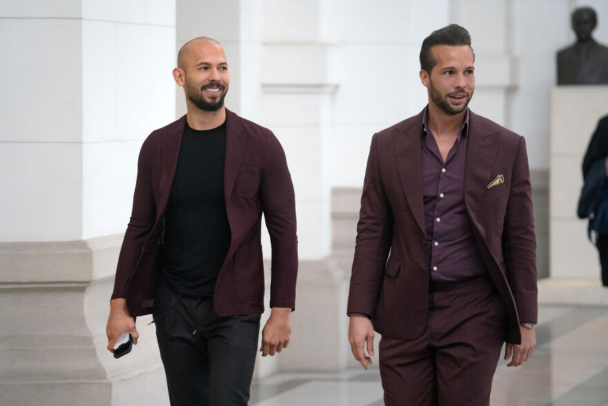 Tate brothers in burgundy outfits walking indoors, representing legal turmoil shaping Tristan Tate&rsquo;s net worth in 2025.