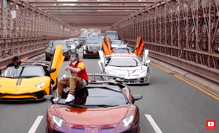 A group of people in luxury Lamborghini cars with scissor doors open, refusing to act like sensible adults on a bridge.