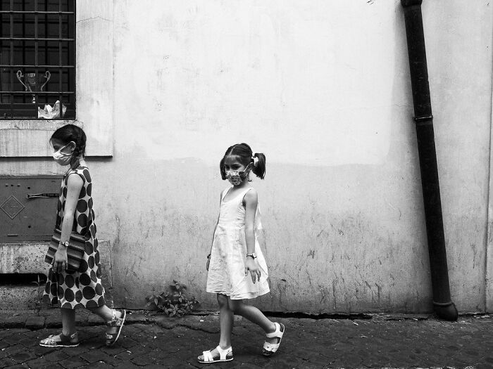 Two young girls wearing masks walk along a weathered wall in a powerful photograph of children of the world.
