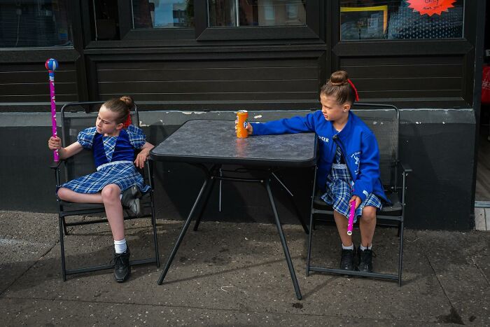 Two children in school uniforms holding colorful batons while sitting outside at a table, captured in powerful photographs.