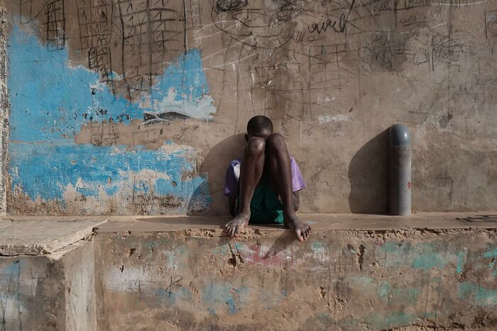 Child sitting alone against a worn wall, captured in a powerful photograph from Children of the World series by Andrea Torrei.
