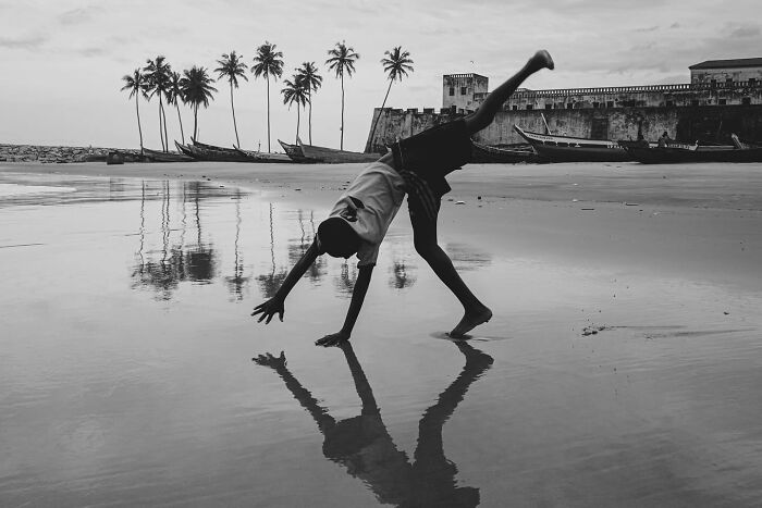 Child doing a cartwheel on a reflective beach at sunset in a powerful photograph of children of the world.